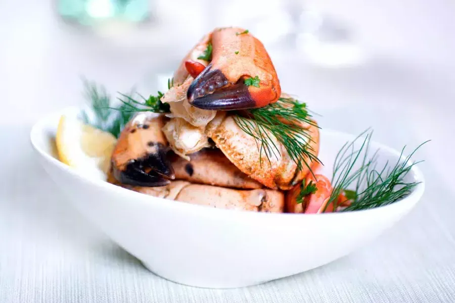 Crab legs 是 stacked in a white bowl and sprinkled with fresh dill.