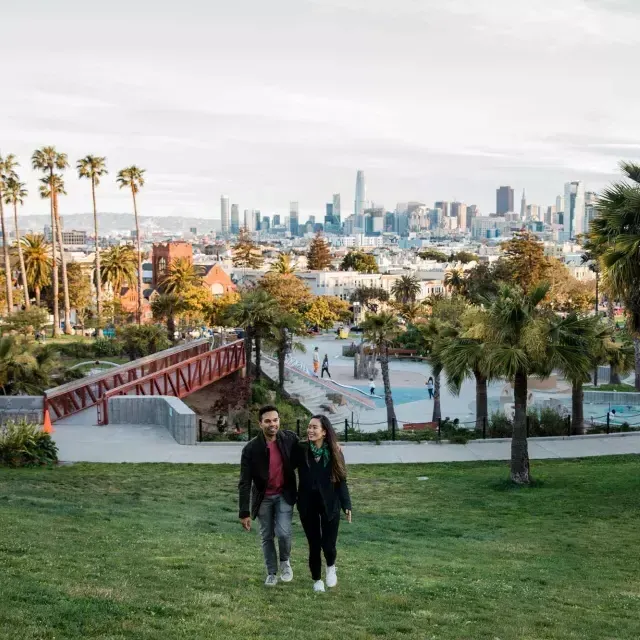 A couple walks toward the camera with 德洛丽丝公园 和 贝博体彩app Skyline behind them.